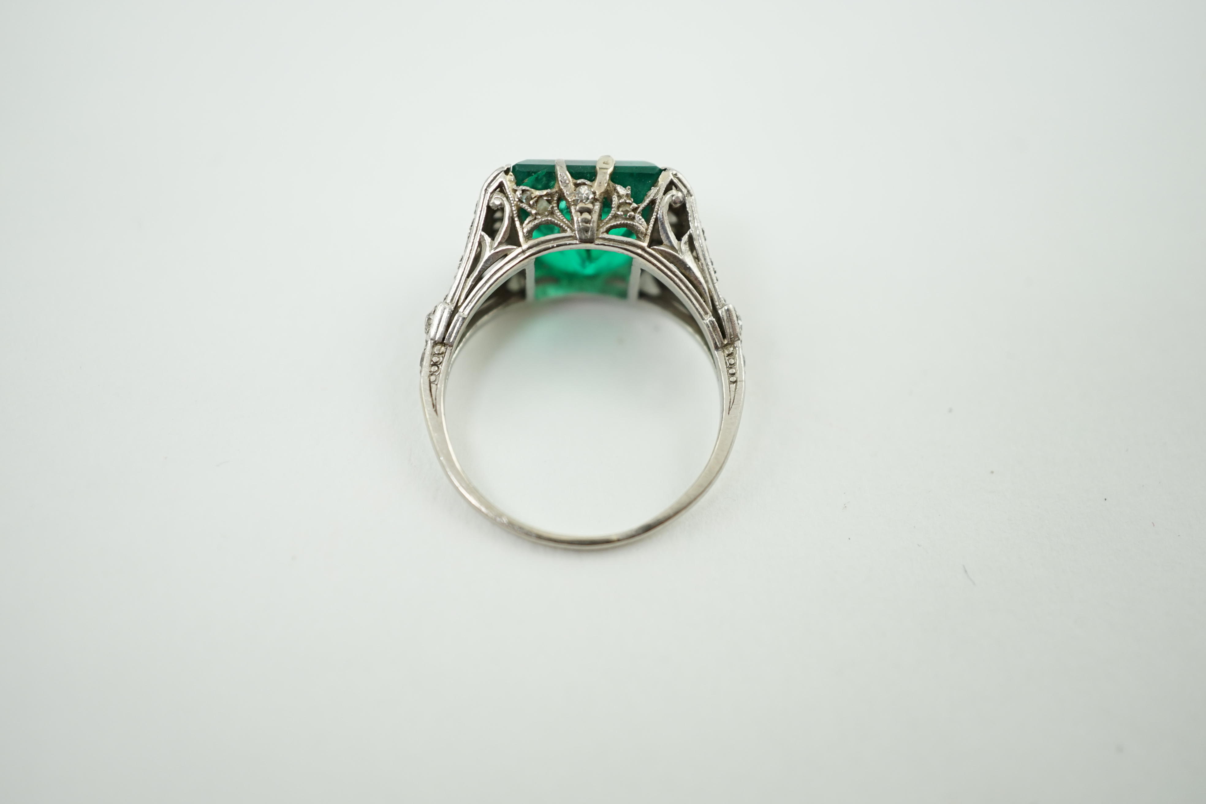 A 1920's/1930's platinum and square cut emerald set dress ring, with pierced and millegrain diamond cluster set shoulders